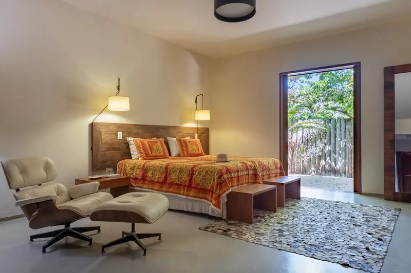 Suíte com cama, poltrona e porta para o jardim